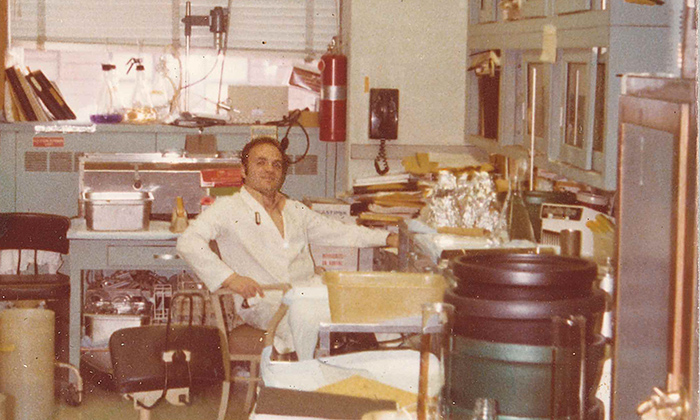 Robert Krug in a lab coat, sitting in his lab in the 1970s