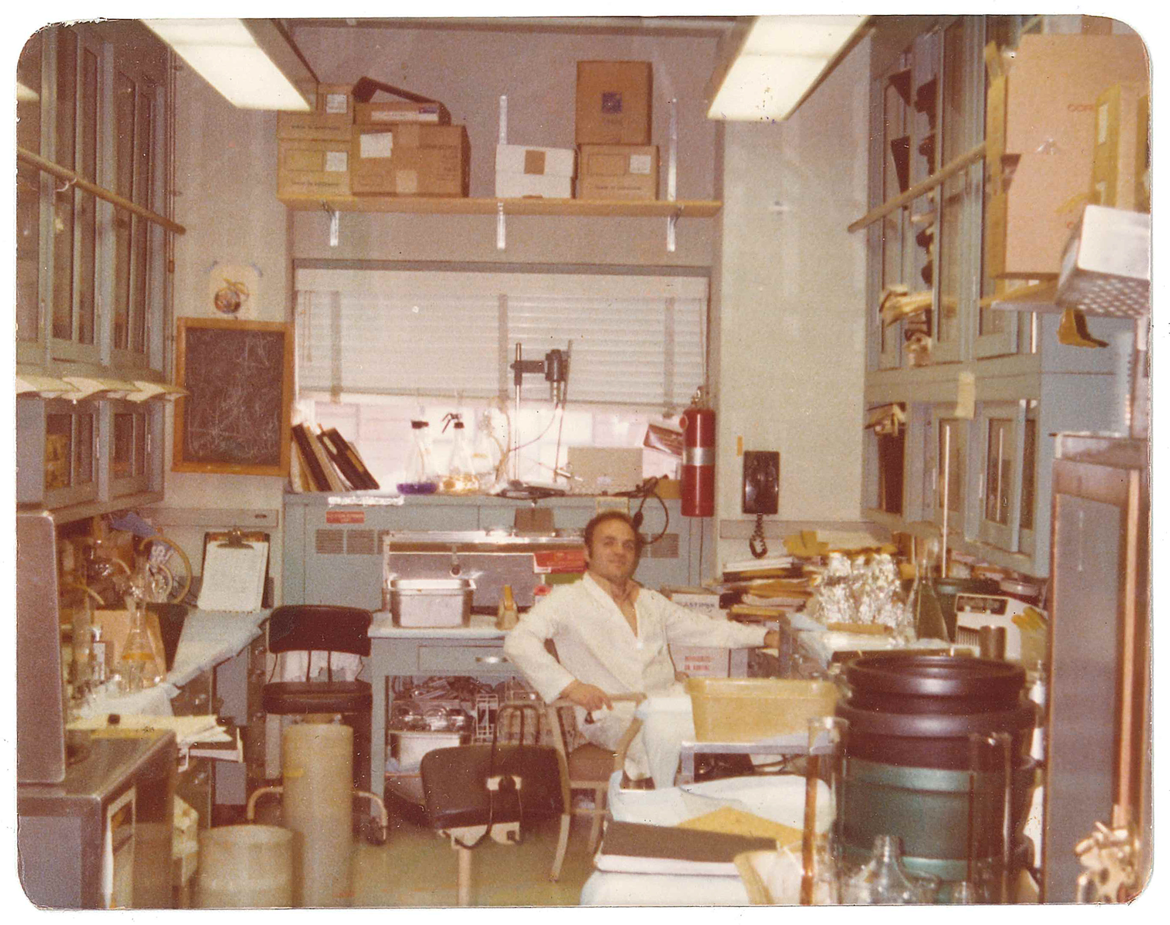 Robert Krug wearing a lab coat, sitting in his lab in the 1970s