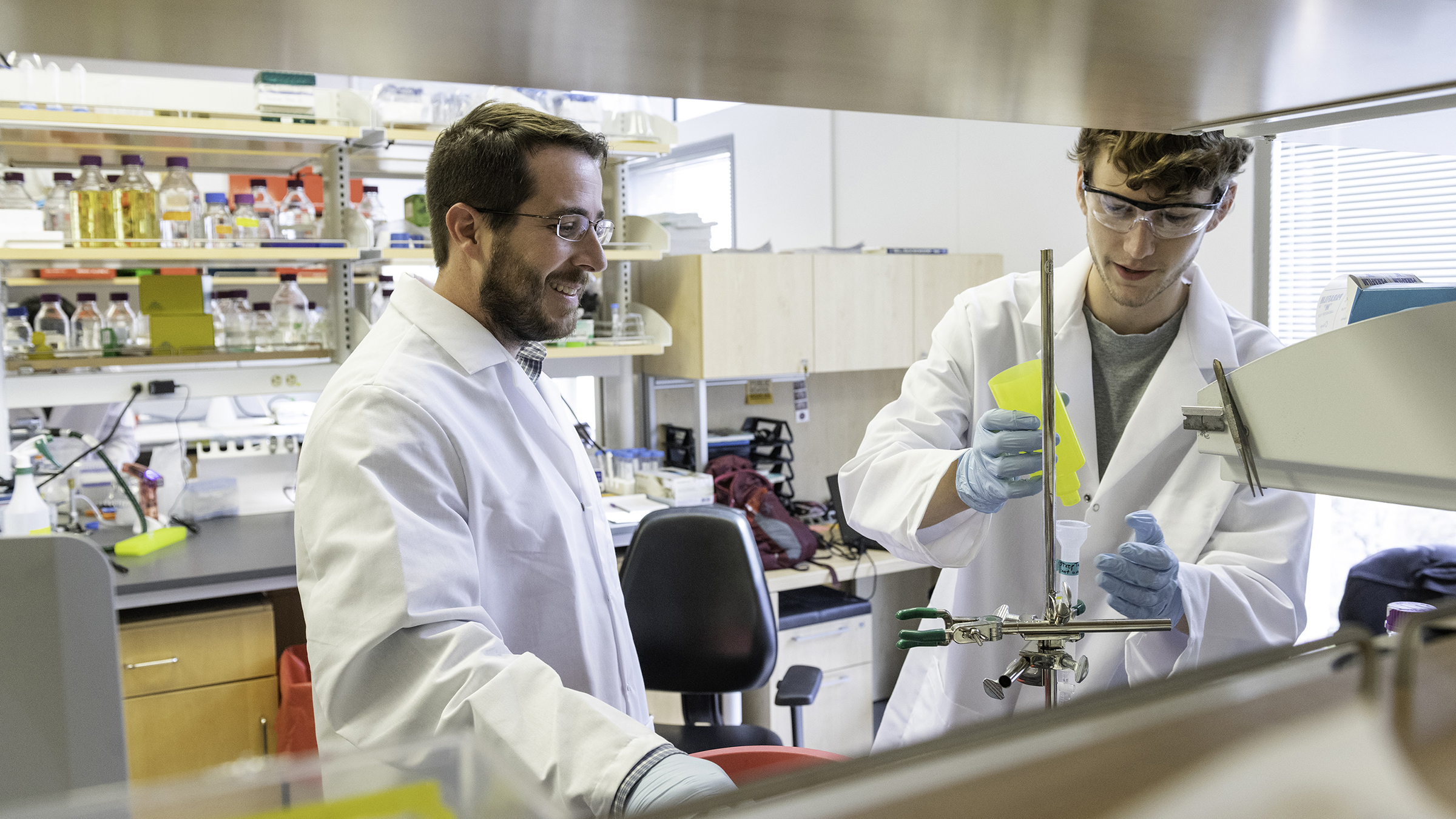 Two scientists in lab coats work at a lab bench.