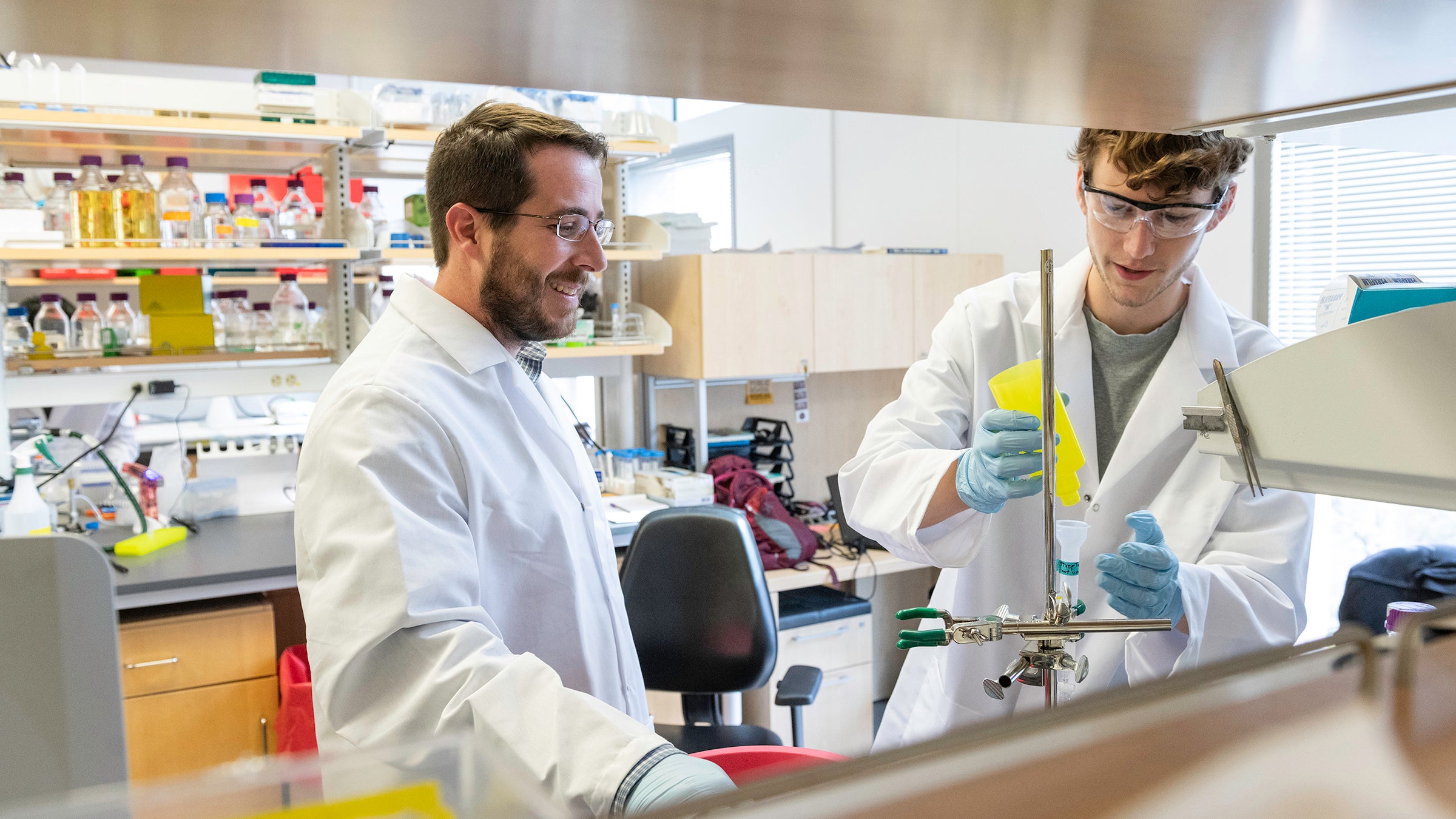 Two scientists in lab coats work at a lab bench.